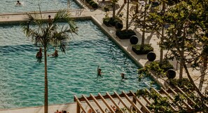 An outdoor swimming pool with people swimming, surrounded by palm trees and a pergola. - Grand Suites Family Resort (Ita)
