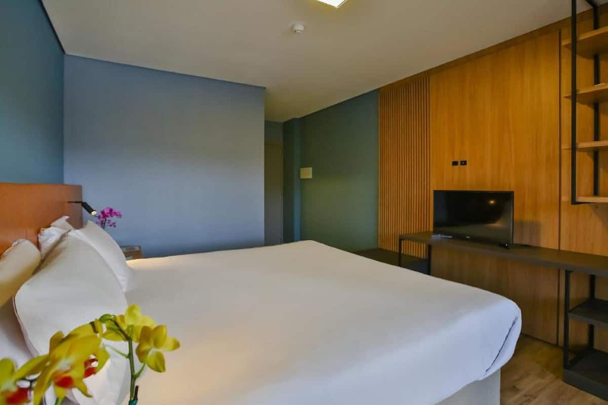 A hotel room with a large bed, a TV, and a wooden panel wall.