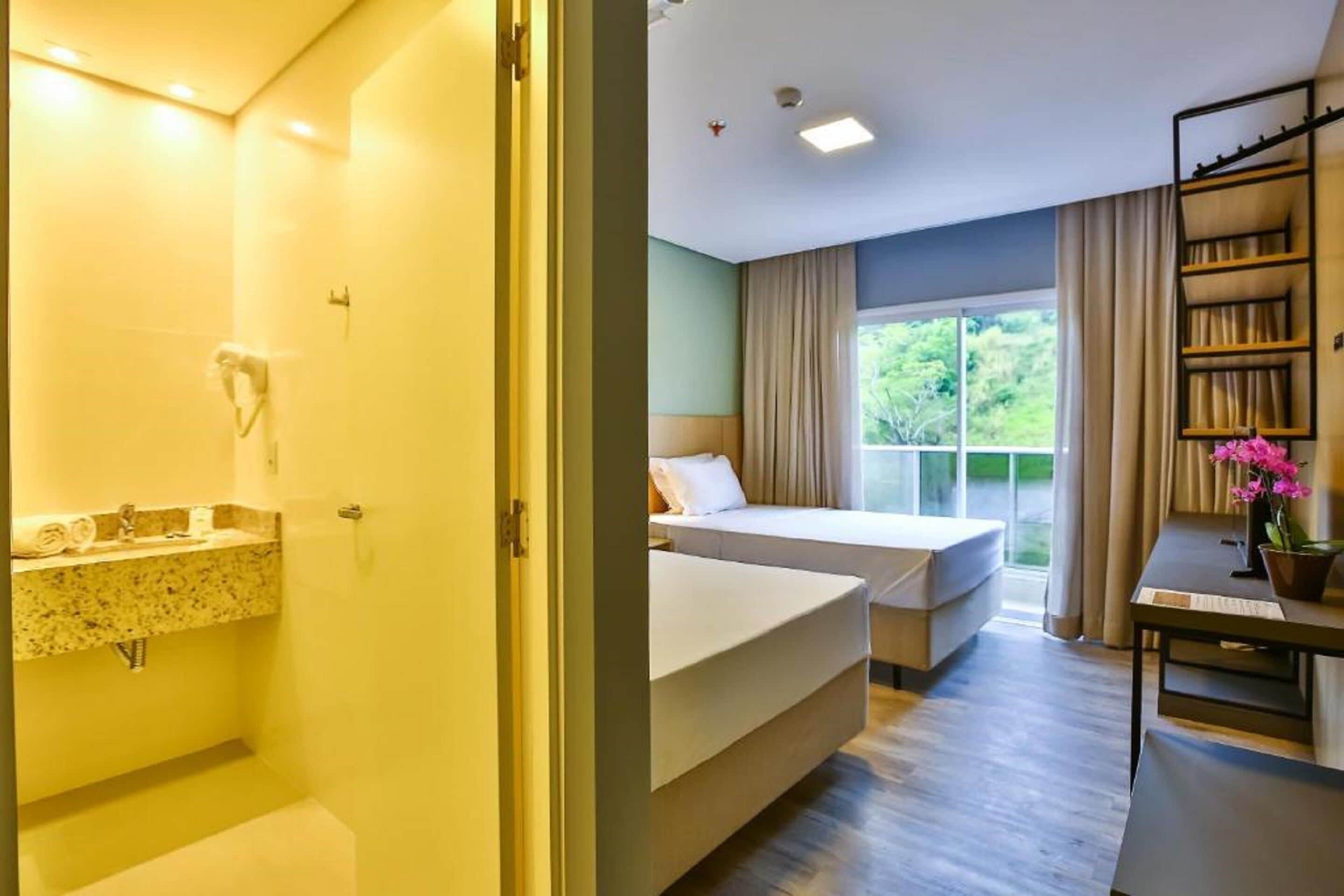 Habitación de hotel con baño, cama, escritorio y ventana con vistas a zonas verdes.