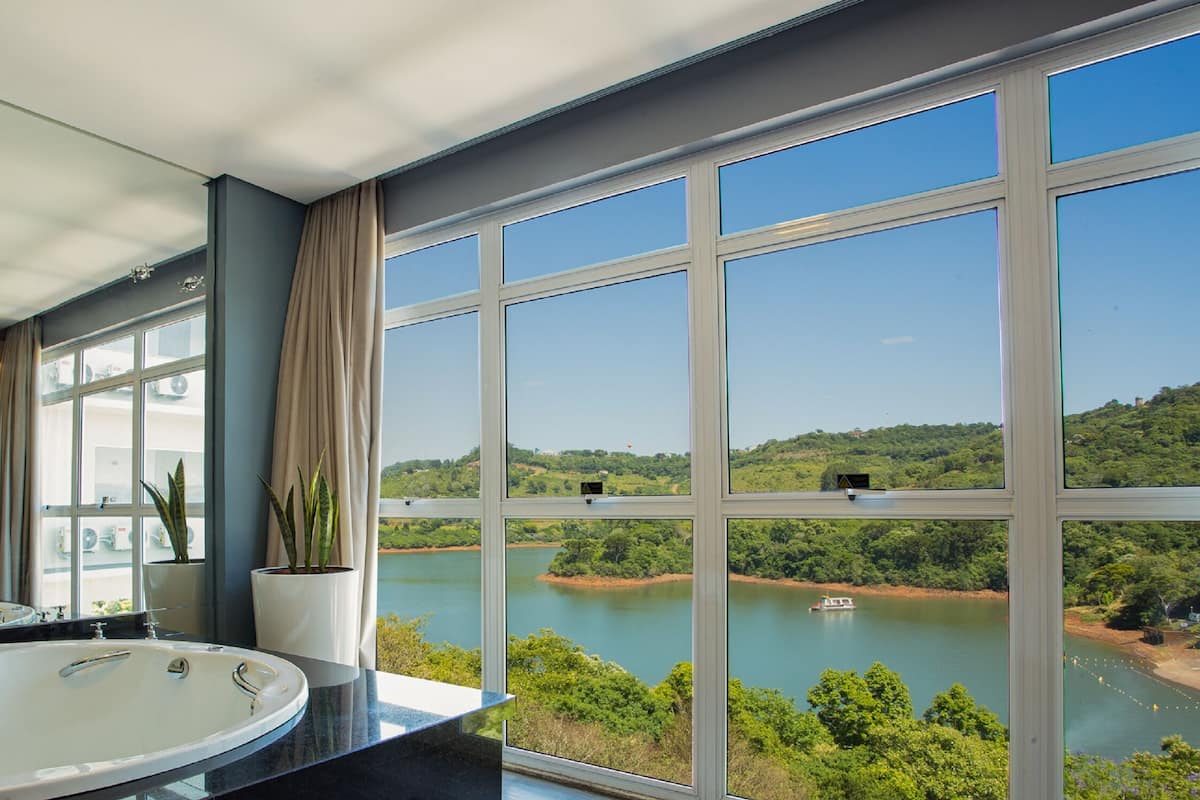 A bathroom with a large bathtub, a sink, and a window offering a view of a lake and greenery.