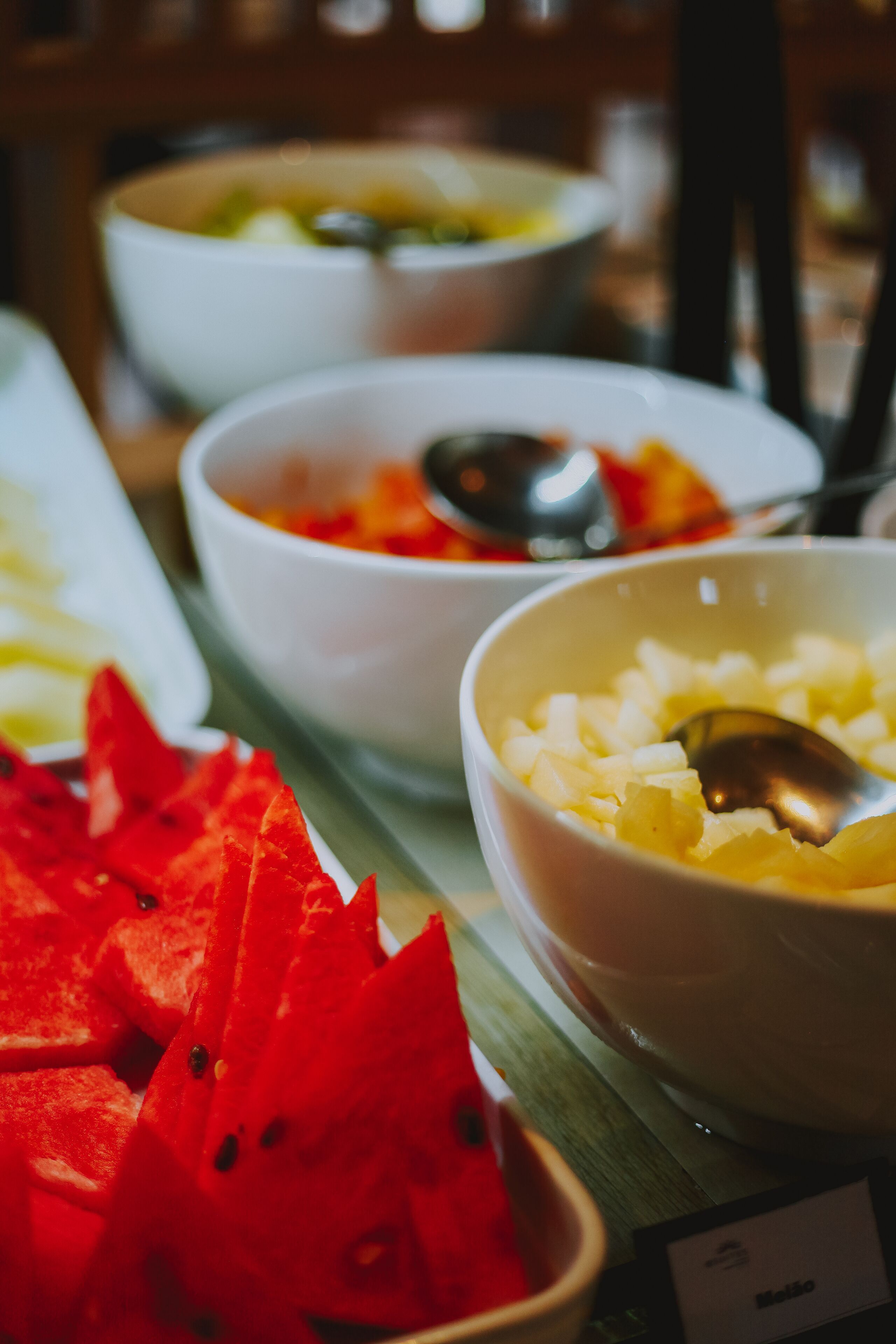 Una mesa de buffet con diversos platos, incluyendo un bol de fruta roja y un bol de comida amarilla, con una cuchara en cada uno.