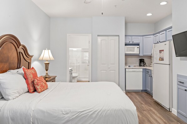 A bedroom with a bed, pillows, a nightstand with a lamp, and a bathroom visible through an open door.
