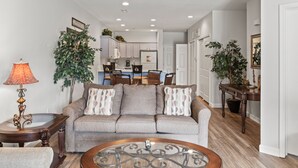 A living room with a sofa, a coffee table, and a lamp. There is a kitchen in the background with cabinets and a refrigerator. - 1 Bedroom Condo + Queen Suite (Adjoined Units, Lock-Off Access) (Branson)