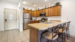 A kitchen with wooden cabinets, a stainless steel refrigerator, a microwave, and a large island with bar stools.