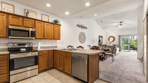 A modern kitchen with wooden cabinets, stainless steel appliances, a dishwasher, and a dining area with a view of the outdoors.