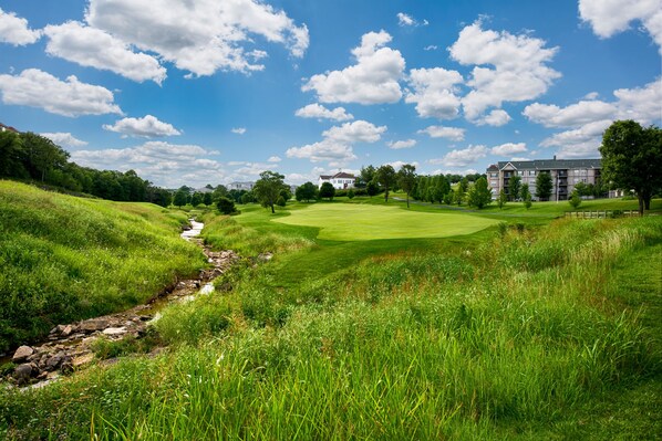 Un parcours de golf avec un ruisseau, un club-house et des immeubles résidentiels en arrière-plan.