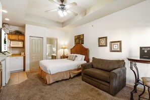 A bedroom with a bed, a brown sofa, a small table, a ceiling fan, and a microwave. - Branson Retreat • Golf View, Kitchenette, & Ticket/Golf Discounts (Branson)