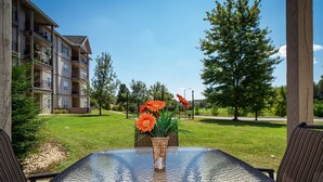 A glass-top table with a potted plant and flowers, surrounded by chairs, in a courtyard with a building in the background. - Central Branson Stay • 1BR/1BA Condo • Walk-In Access (Branson)
