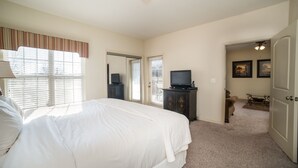 A bedroom with a large bed, a dresser, a television, and a door leading to another room. - Central Branson Stay • 1BR/1BA Condo • Walk-In Access (Branson)