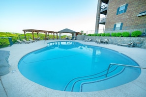 A swimming pool with lounge chairs and a gazebo, surrounded by a brick building.