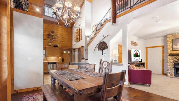 Un comedor espacioso con una mesa y sillas de madera, un candelabro y una escalera que sube a un nivel superior.