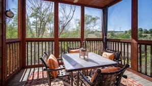 Un patio techado con mesa y sillas, un ventilador de techo y vistas a árboles y paisaje.