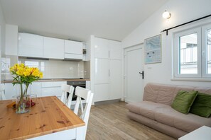 Una cocina moderna con armarios blancos, una mesa de comedor con sillas y un sofá beige con cojines verdes.