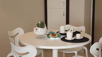 Een ronde tafel met witte stoelen, een glazen vaas met bloemen, een bord koekjes en witte kopjes en schotels.