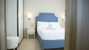 A bedroom with a blue bed, white bedding, a small bedside table, and wall-mounted lights. - 2-bedroom DELUXE apartment (Rimini)
