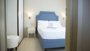 Een slaapkamer met een blauw bed, witte beddengoed, een klein nachtkastje en wandlampen.