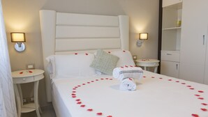 A hotel room with a neatly made bed, a bedside table, a small round table, and a wardrobe. - 2-bedroom DELUXE apartment (Rimini)
