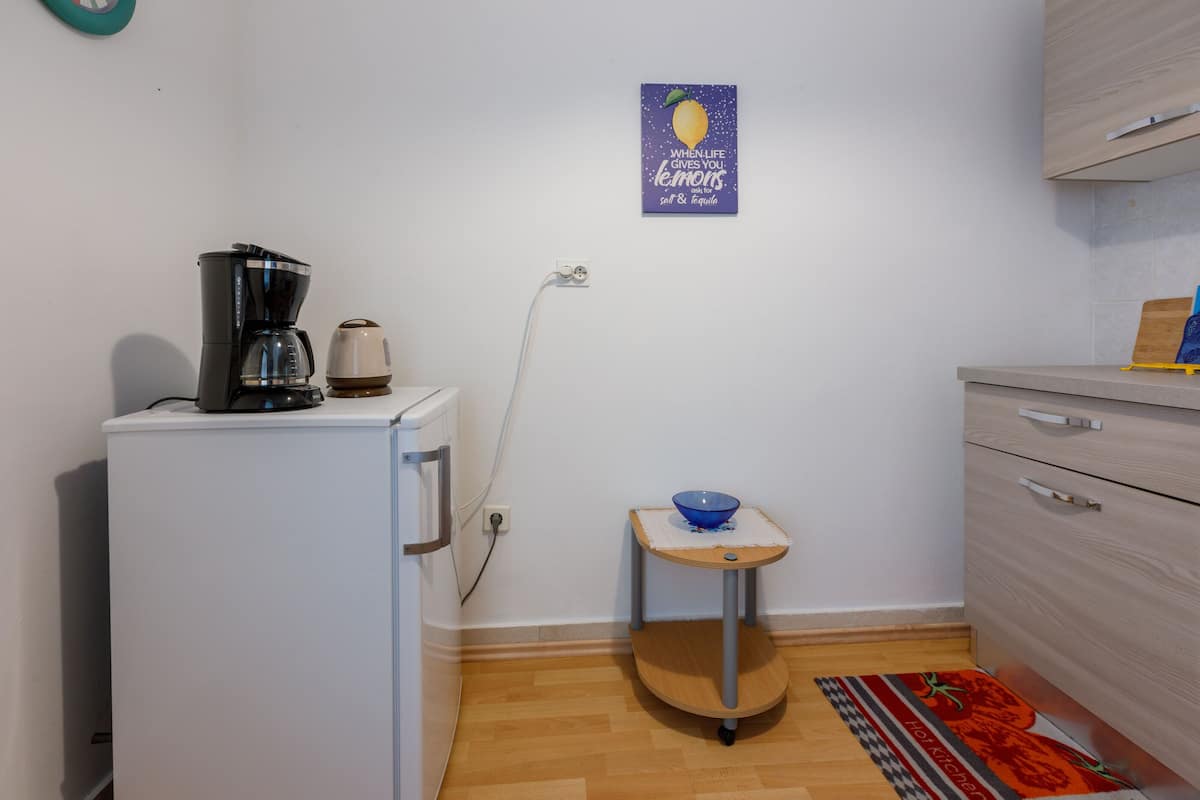 Una cocina compacta con cafetera, una mesita con un tazón y un cuadro en la pared.
