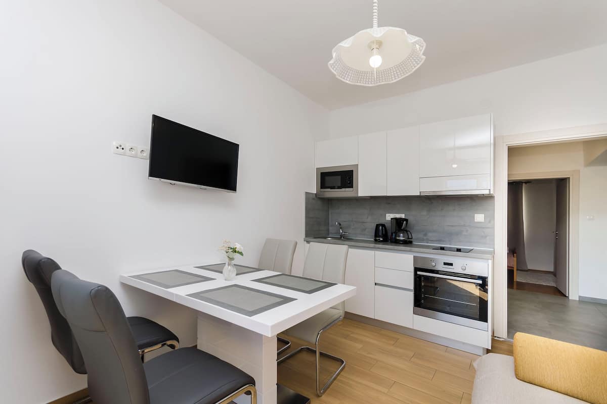 Eine moderne Küche mit Flachbildfernseher, weißen Schränken, einer Mikrowelle und einem Backofen.