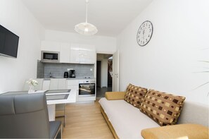 A modern kitchen with white cabinets, a microwave, and an oven. There is a dining table with chairs and a sofa with patterned cushions. - Apartments Baldo (Vodice)