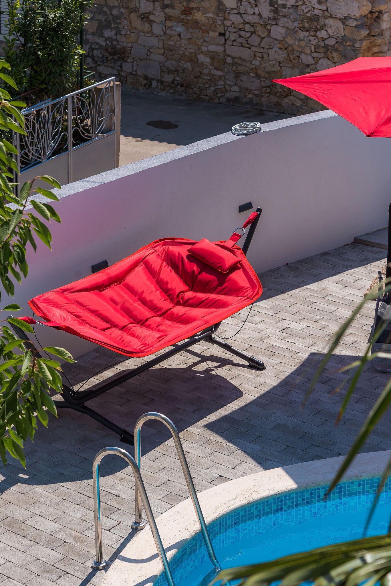 Un espace extérieur rouge avec des sièges, une piscine et un mur de pierre en arrière-plan.