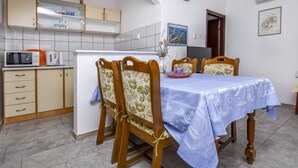 Un comedor con una mesa dispuesta para cuatro, sillas de madera, una cocina al fondo y un reloj en la pared.