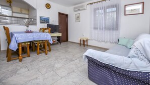 Una sala de estar con sofá, una mesa de comedor con sillas, una zona de cocina y un ventanal con cortinas.