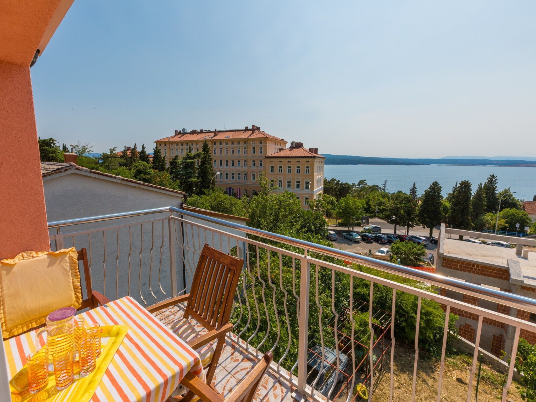 En balkon med et bord og stole, udsigt over vand og en stor bygning.