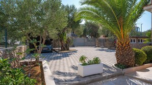 A paved courtyard with a palm tree, a white planter with plants, and a stone wall. - House Villa Fox (Kanica)
