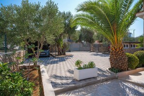 A paved courtyard with a palm tree, a white planter with plants, and a stone wall. - House Villa Fox (Kanica)