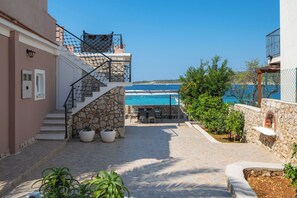 A stone staircase leading to a pool area with outdoor furniture, surrounded by greenery and overlooking a clear blue sea.