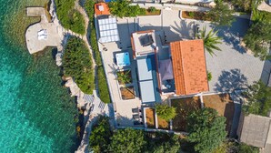 Vista aerea di una proprietà costiera con piscina, lettini e tetto in tegole.