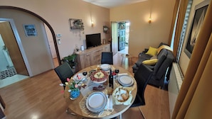 A dining area with a round table set for four, a television, and a sofa. - Apartment Delost (Lovran)