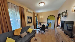 A modern living room with a grey sofa, a small round coffee table, and a TV on a wooden cabinet. - Apartment Delost (Lovran)