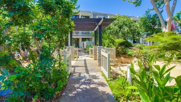 A pathway leading to a modern building with a covered entrance, surrounded by lush greenery and trees. - Beachfront 1BR Condo | Pool | Hot Tub | Sleep 4 (Oceanside)