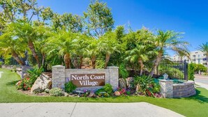 A sign for North Coast Village with a landscaped garden and palm trees. - Beachfront 1BR Condo | Pool | Hot Tub | Sleep 4 (Oceanside)