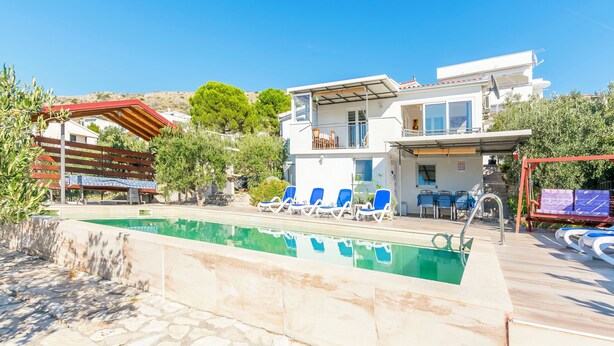 A modern two-story building with a swimming pool, outdoor seating, and a view of the surrounding landscape. - House Osti (Rogoznica)