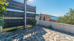 A stone-paved outdoor area with a metal gate, a clear blue sky, and a view of the sea in the background. - House Osti (Rogoznica)