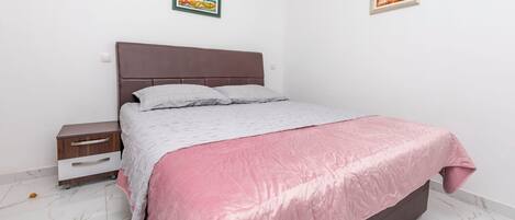 A bedroom with a bed, a nightstand, a drawer unit, and two framed pictures on the wall.