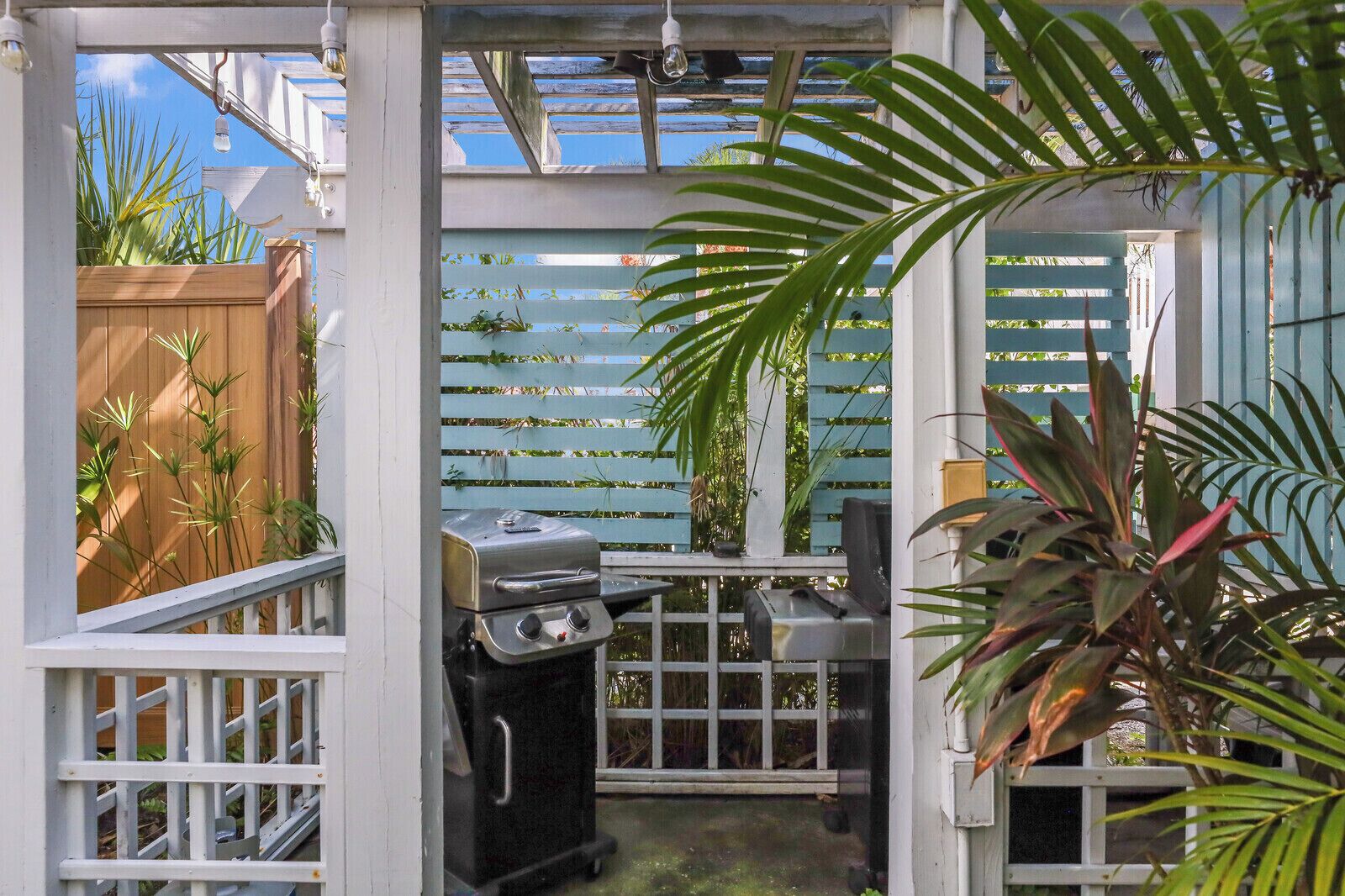Eine Terrasse mit Grill, Holzzaun und verschiedenen Pflanzen.