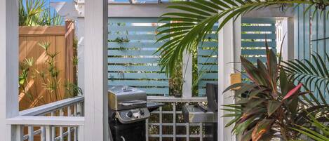 Eine Terrasse mit Grill, Holzzaun und verschiedenen Pflanzen.