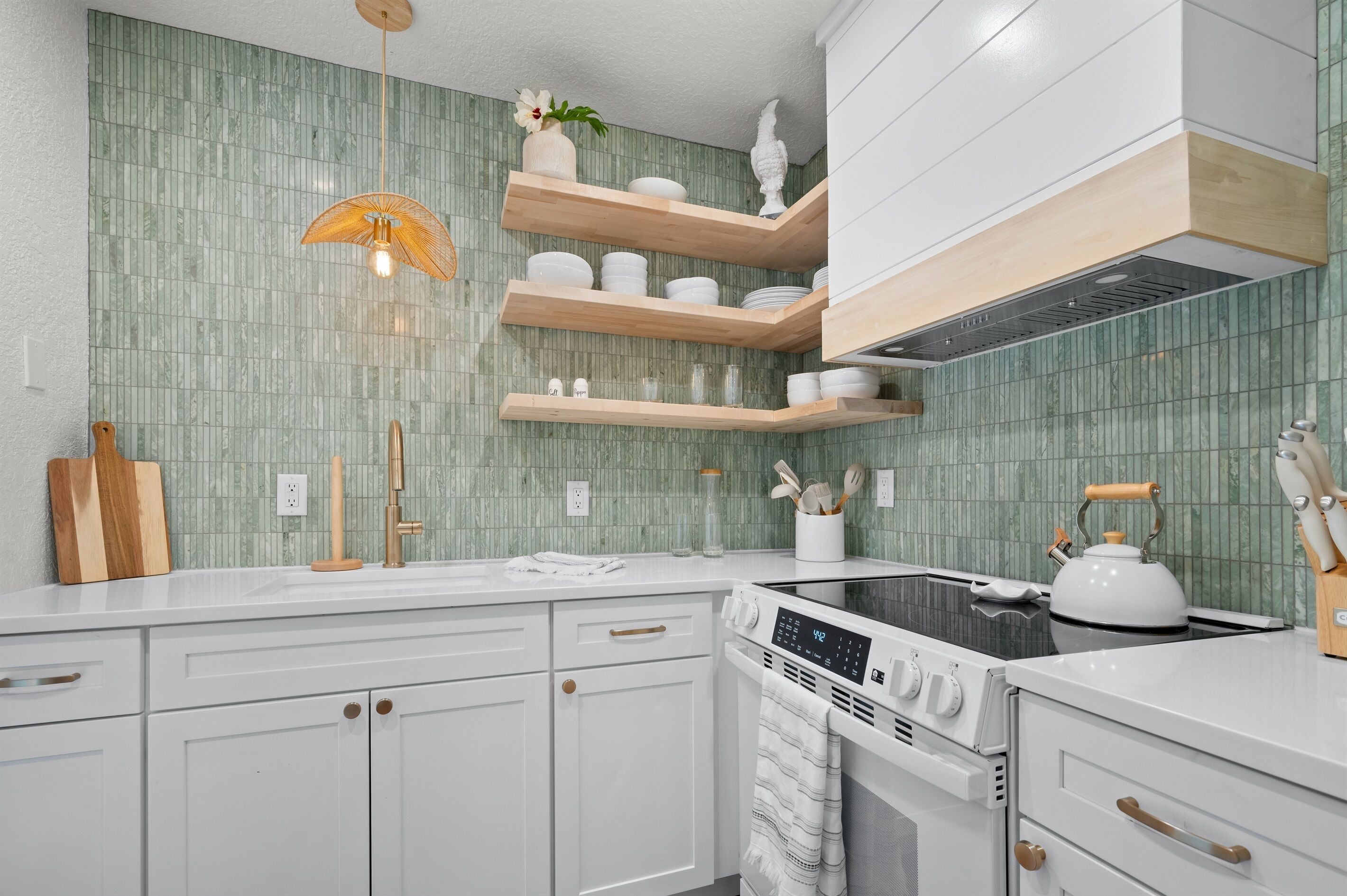 Une cuisine moderne avec des meubles blancs, une cuisinière encastrée et un dosseret de carrelage vert.