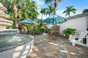 Une terrasse en pierre avec une fontaine, des sièges d’extérieur et des parasols.