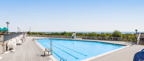 Relax by the pool surrounded by lounge chairs and umbrellas, with a lifeguard on duty.