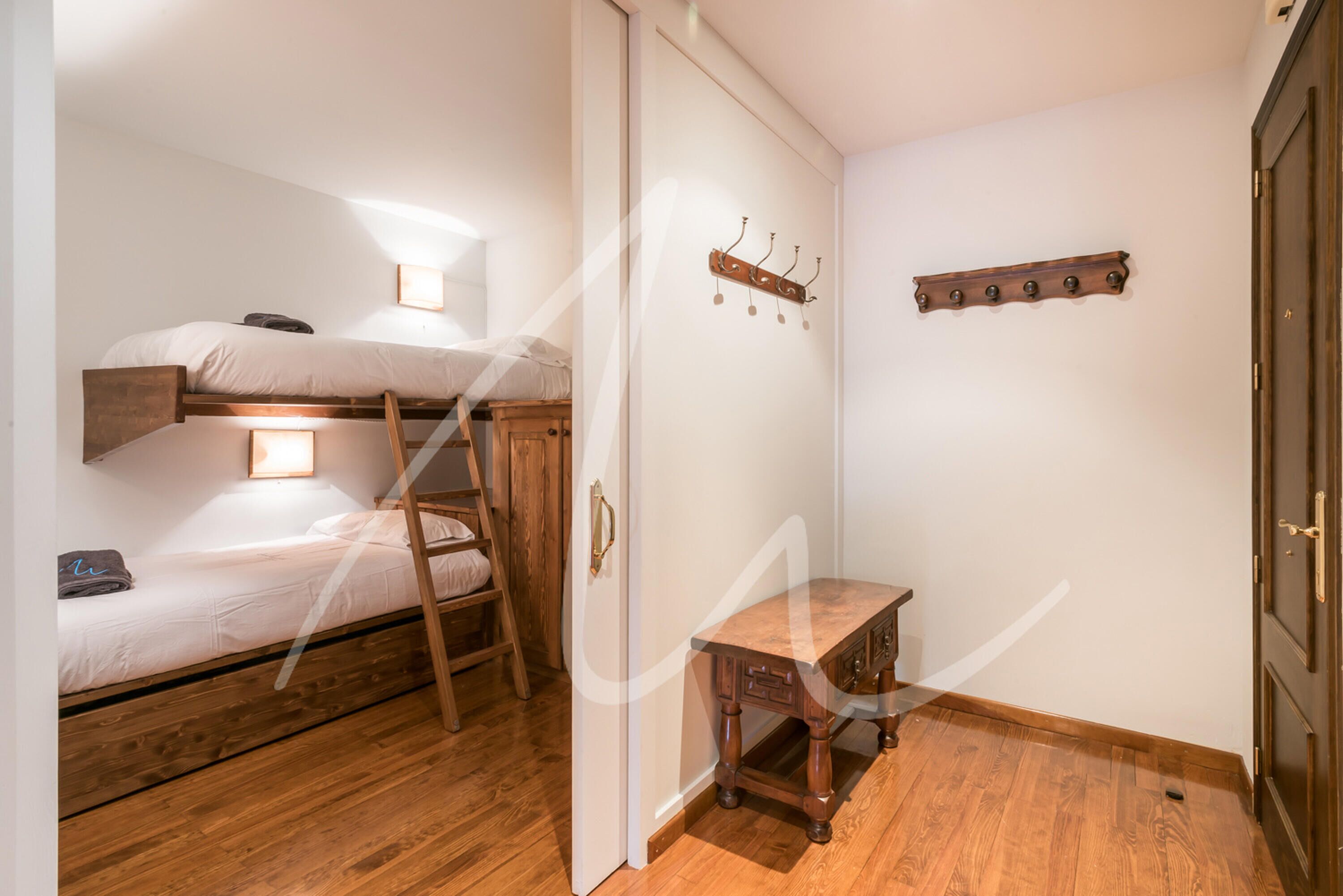 Une pièce avec un lit superposé, une petite table en bois, une échelle et un porte-manteau.