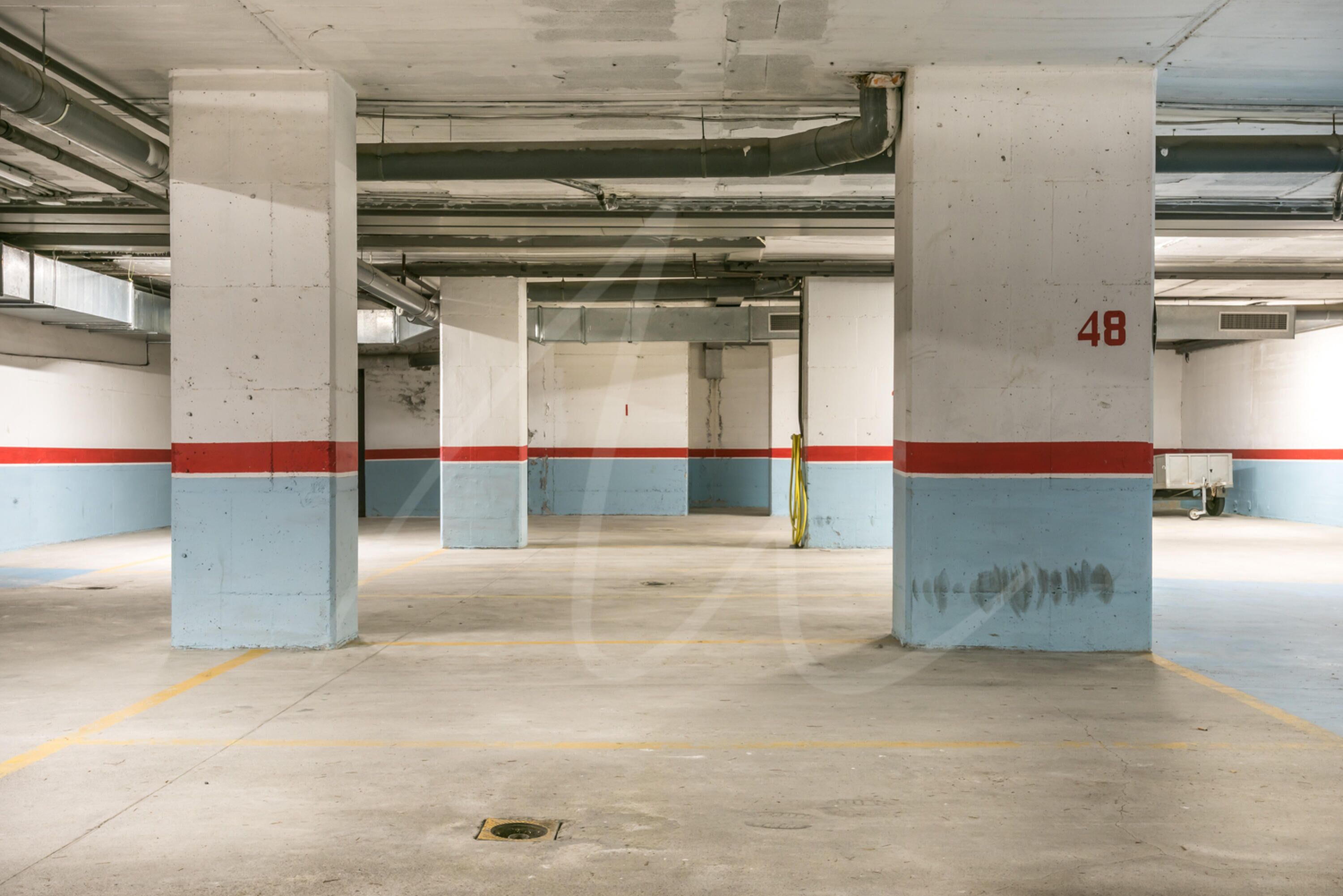 A parking garage with concrete pillars, yellow lines on the floor, and a red and blue stripe along the walls.