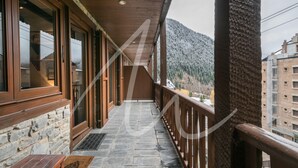 A wooden balcony with stone flooring, wooden railings, and a view of snow-covered mountains.