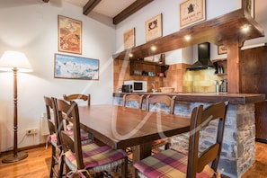 Uma mesa de jantar de madeira com seis cadeiras, uma área de cozinha com micro-ondas e um espaço para café.