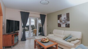 Ein Wohnzimmer mit einer Couch, einem Couchtisch mit Obst, einem Fernseher und einer Glastür zum Garten.
