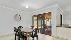 A dining area with a round table and chairs, a kitchen with white cabinets, and a sliding glass door leading to an outdoor patio. - Mandurah Estuary Breeze (Wannanup)